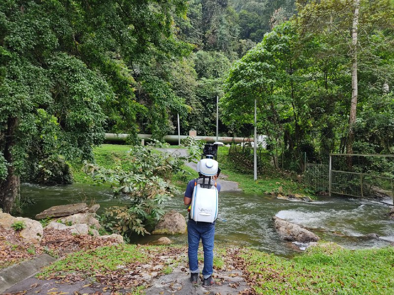 A man doing data collection in nature, about to cross a river with a LiDar Backpack on