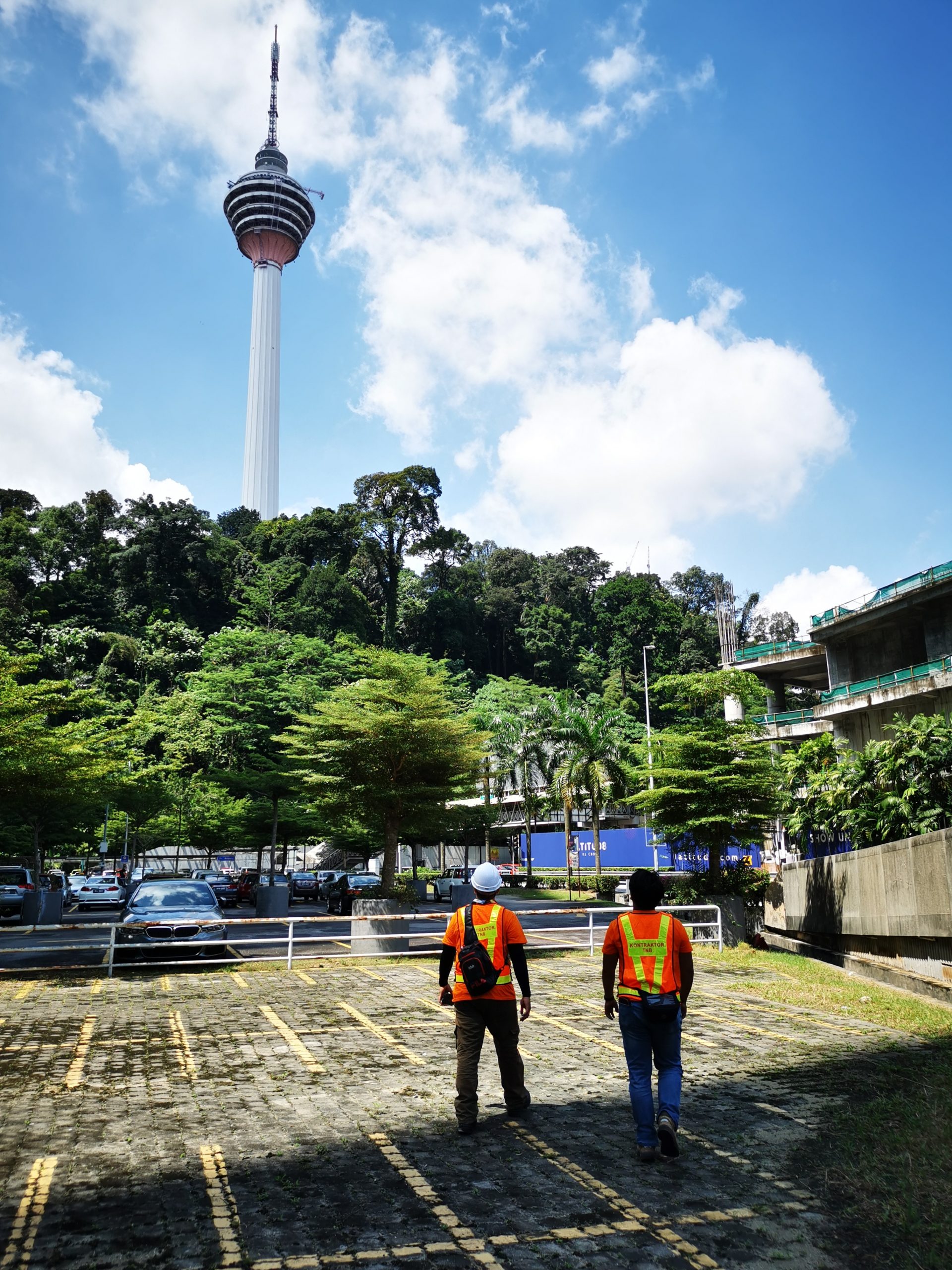 two men in safety vest looking at Kuala Lumpur tower in the distant